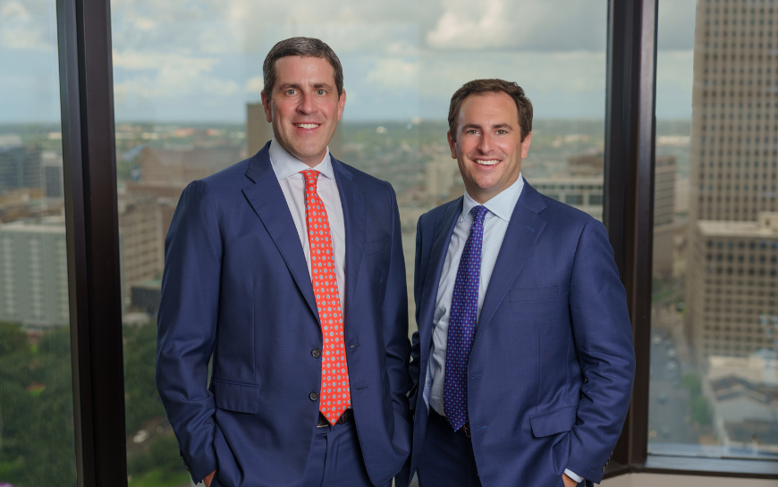 Two attorneys from Huber Thomas Law standing together in front of a large window with a cityscape in the background, representing the firm’s professional and approachable legal team.